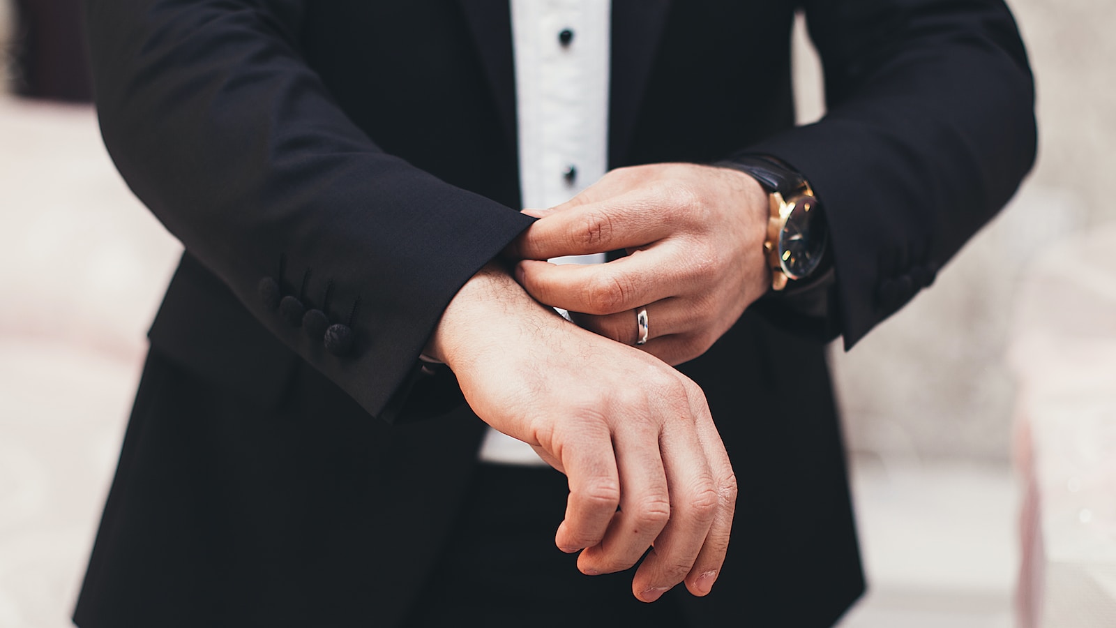 A man's hands adjusting the cuffs of his black suit